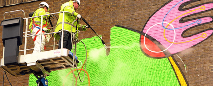 two technicians cleaning graffiti with a pressure washing machine